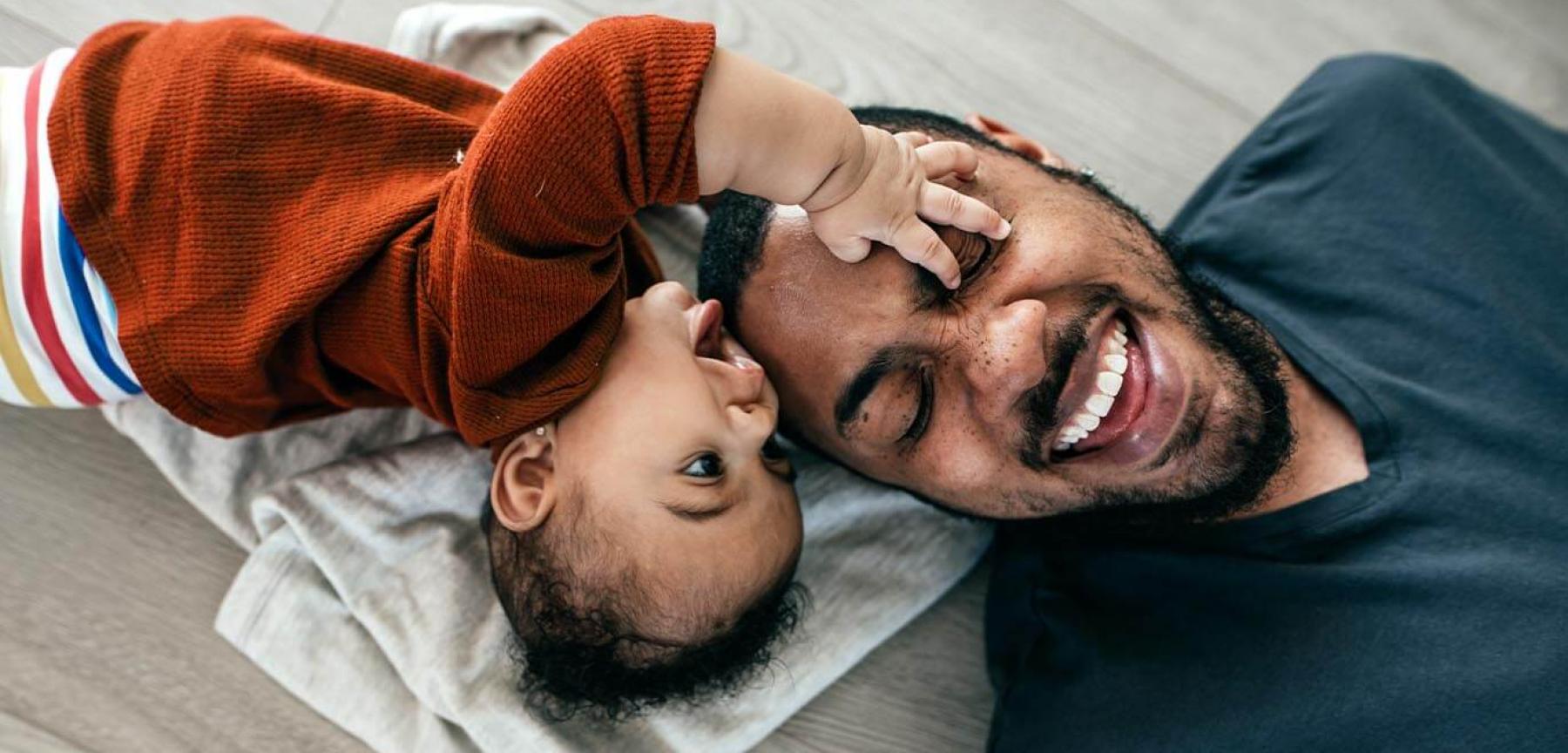 Dad and baby daughter laughing while playing on the ground