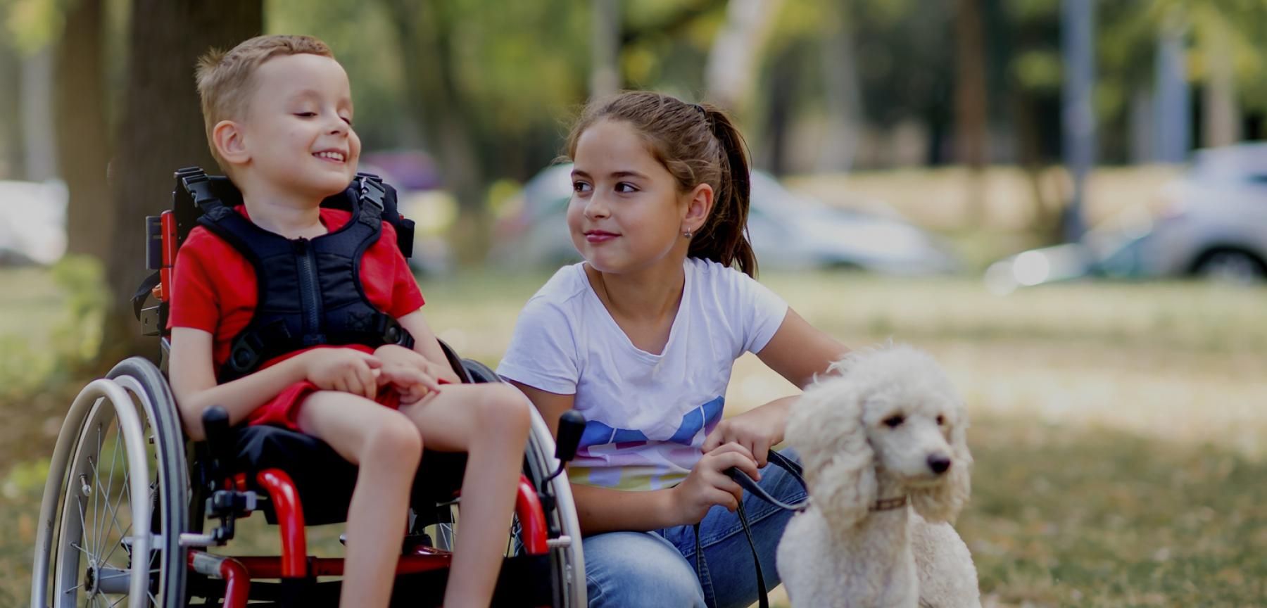 little boy in wheelchair with sister staring at him while holding their pet dog